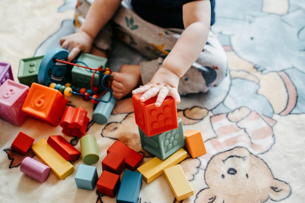 Kleinkind engagieren sich mit lebendigen Spielzeugblöcken auf einem gemusterten Teppich in einer spielerischen Umgebung.